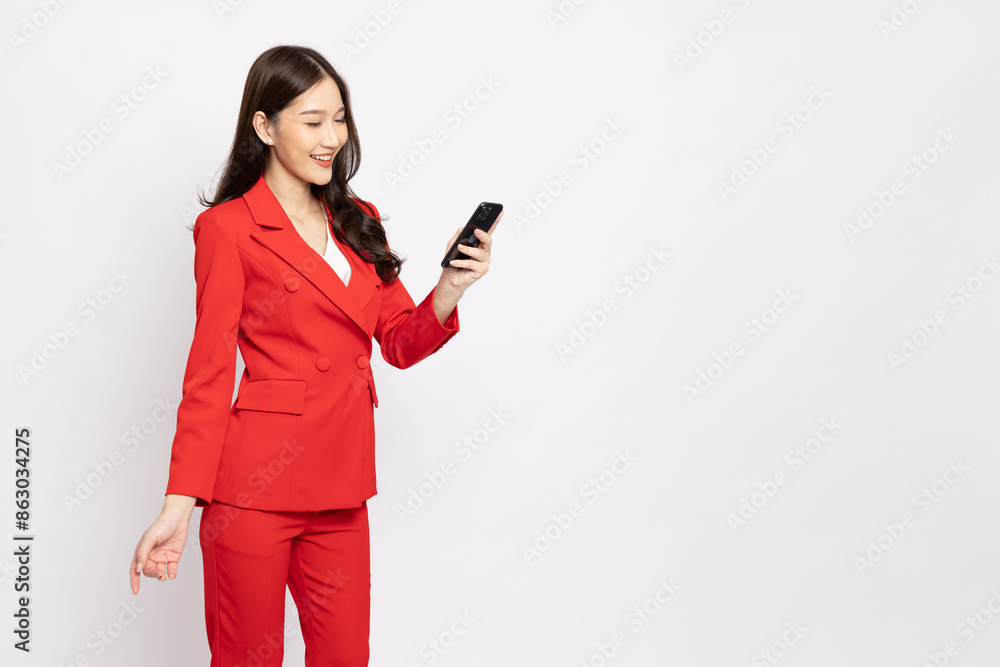 Happy Asian businesswoman in red suit typing and using mobile phone isolated on white background Happy Asian businesswoman in red suit typing and using mobile phone isolated on white background