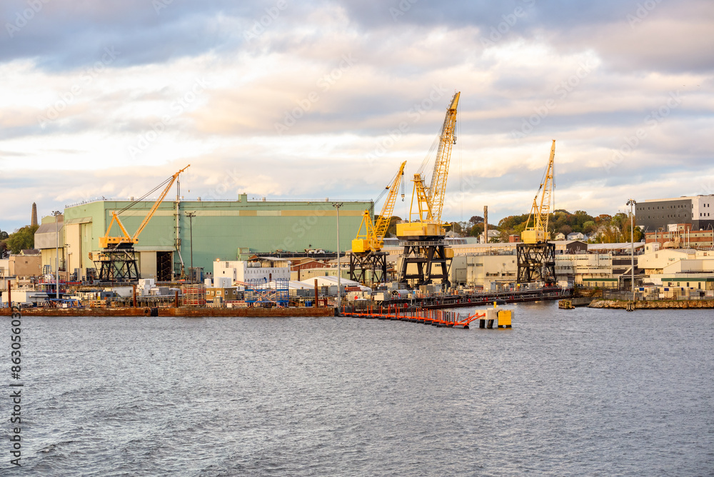 Fototapeta premium Quayside manufacturing plant with large yellow port cranes on the bank of a river at sunset in autumn