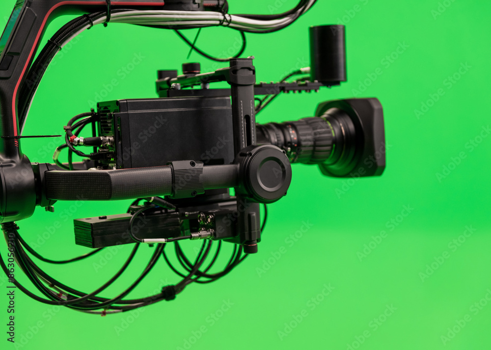 Black camera on carbon jib crane against green background. TV studio interior with green screen. Video production with background replacement. Black camera on carbon jib crane against green background. TV studio interior with green screen. Video production with background replacement.