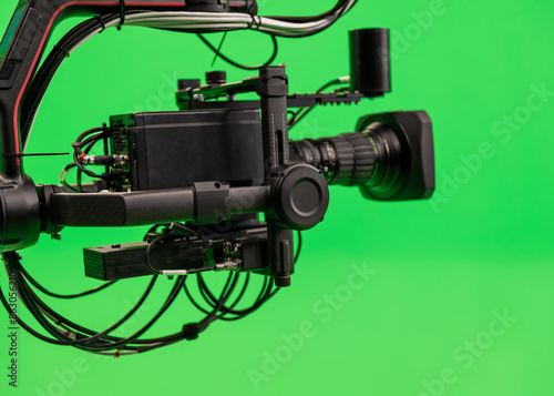 Black camera on carbon jib crane against green background. TV studio interior with green screen. Video production with background replacement.