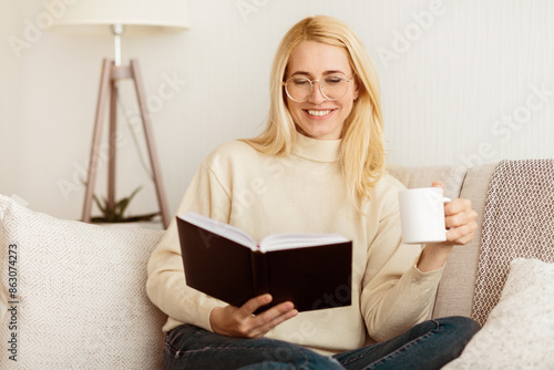 Woman Reading Book And Drinking Tea, Having Rest At Home On Sofa © Prostock-studio