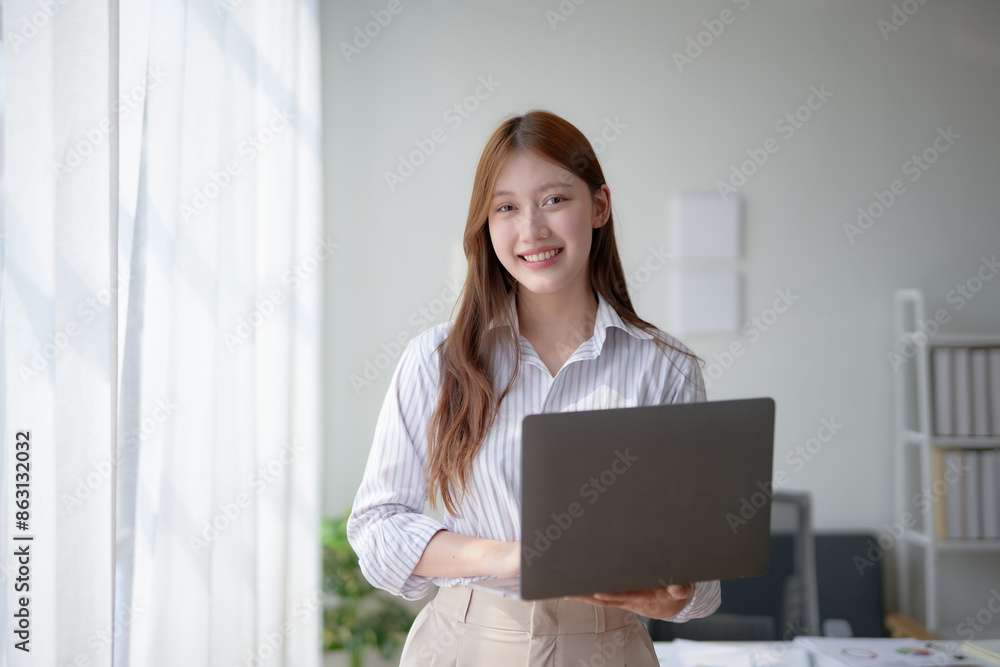 Young businesswoman with a laptop, smiling confidently in a modern office space with natural light from large windows, ready for work. Young businesswoman with a laptop, smiling confidently in a modern office space with natural light from large windows, ready for work.
