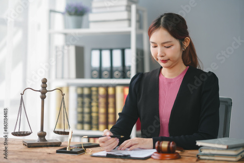 Professional female lawyer working at her desk with legal documents, scales of justice, and gavel in a modern office setting.