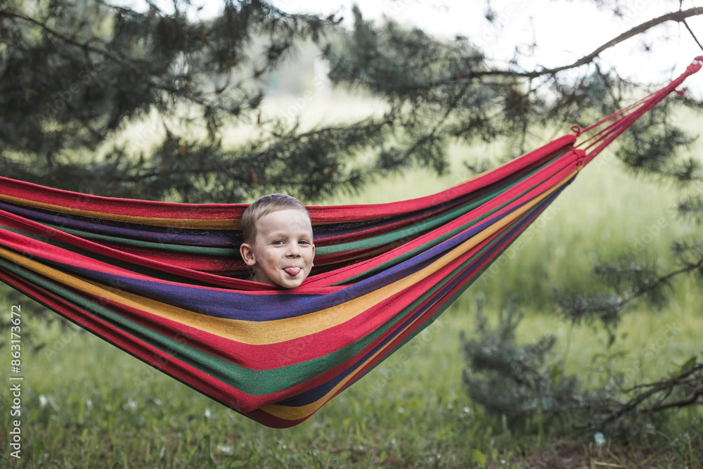 Summer holidays for children in the fresh air.. A cute little boy is having fun with a colorful hammock in the backyard. A child in a hammock. Summer holidays for children in the fresh air.. A cute little boy is having fun with a colorful hammock in the backyard. A child in a hammock.