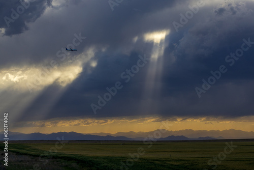 An airplane flying in the stormy sky above the Colorado prairies with the Rocky Mountains visible in the distance