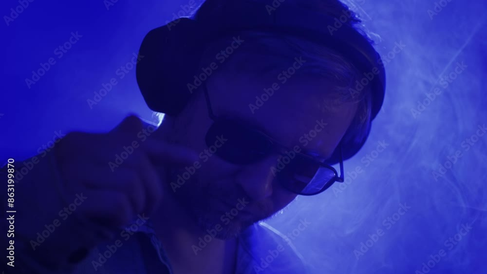 DJ playing music on festival in night club. Techno musician with headphones and sunglasses performing at nightclub for concert crowd of people, city bar. DJ playing music on festival in night club. Techno musician with headphones and sunglasses performing at nightclub for concert crowd of people, city bar.
