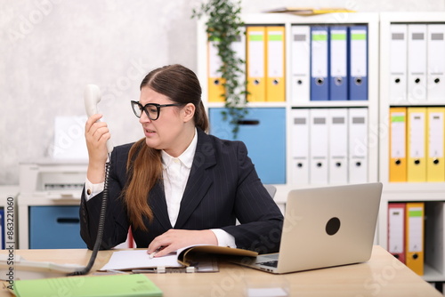 Sekretärin im schwarzen Business Anzug sitzt am Schreibtisch und legt sich mit Gesprächspartner an photo