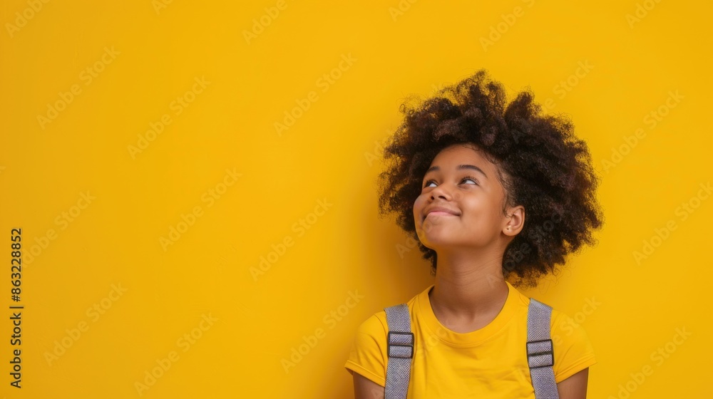 A cheerful smiling black little boy with a backpack is having fun on the background of a yellow wall and points to your text. The concept of the school. back to school. A cheerful smiling black little boy with a backpack is having fun on the background of a yellow wall and points to your text. The concept of the school. back to school.