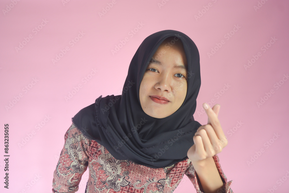 Portrait of young Asian Muslim woman with pointing gesture on pink background Portrait of young Asian Muslim woman with pointing gesture on pink background