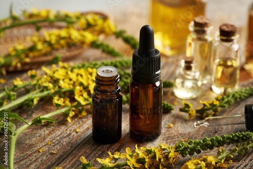 Dark bottles of aromatherapy essential oil with blooming agrimony plant