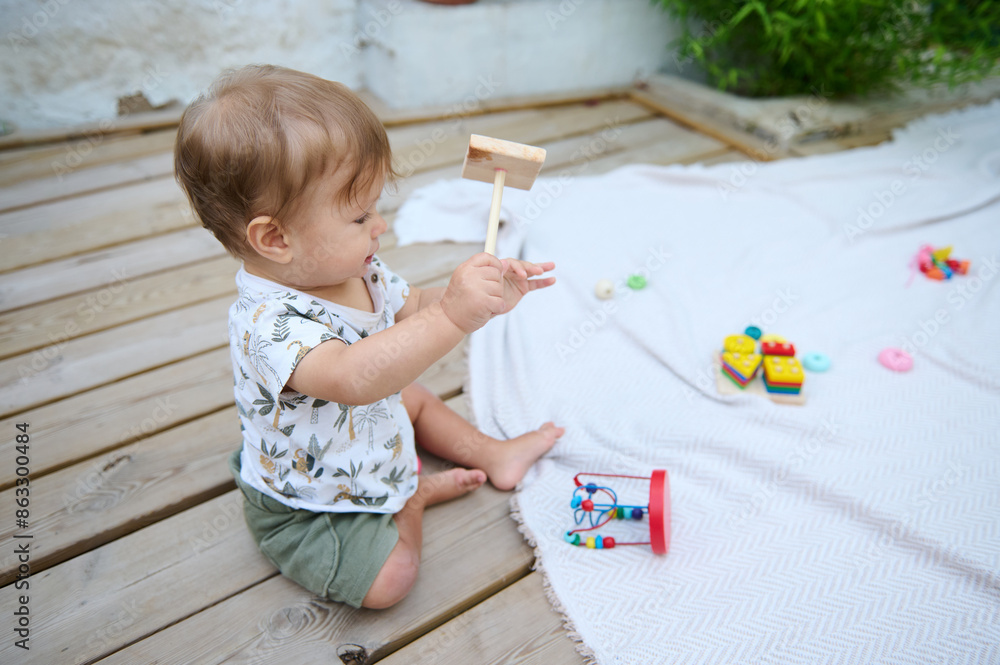 Cute baby playing with wooden toy hammer on outdoor deck Cute baby playing with wooden toy hammer on outdoor deck
