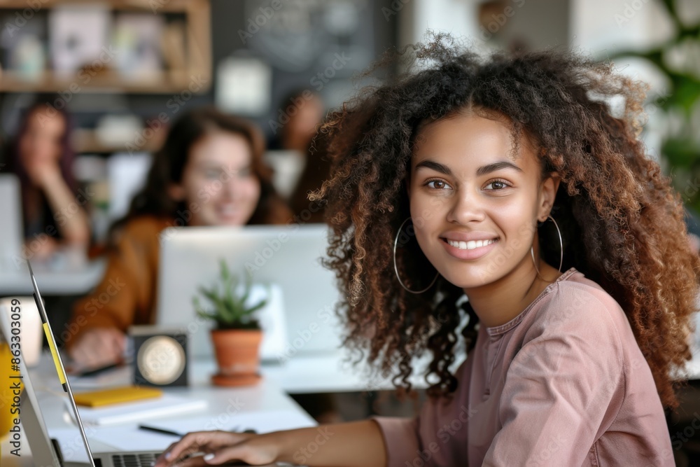 A young woman with curly hair smiling while editing on her computer in a modern, well-lit office environment. Colleagues working in the background. A young woman with curly hair smiling while editing on her computer in a modern, well-lit office environment. Colleagues working in the background.