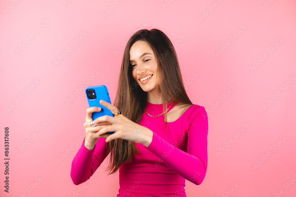 Smiling charming brunette woman use mobile phone happy texting, chatting, messaging in social networks addicted to modern technologies isolated over pink background. Online communication. Smiling charming brunette woman use mobile phone happy texting, chatting, messaging in social networks addicted to modern technologies isolated over pink background. Online communication.
