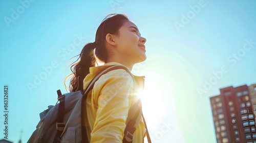 Young woman with backpack standing against clear sky in city during sunny day