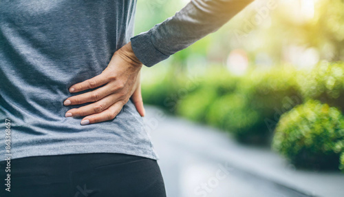 woman's hand holding her lower back, signifying back pain. The image is in macro focus, with a clean, blurred background, highlighting the discomfort