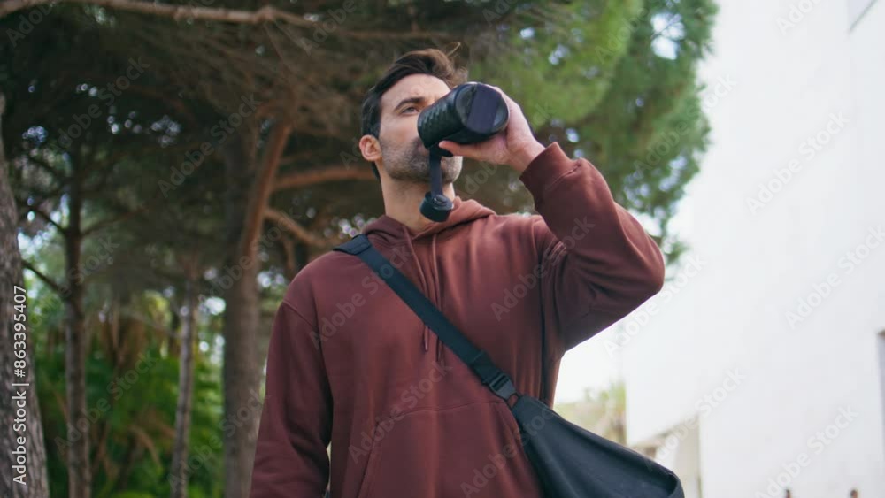 Handsome sportsman drinking bottle after training outdoors. Hispanic guy walking Handsome sportsman drinking bottle after training outdoors. Hispanic guy walking
