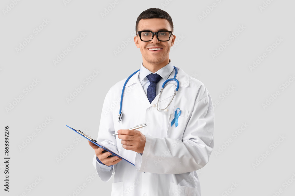 Male urologist with blue ribbon writing in clipboard on light background. Prostate cancer awareness concept Male urologist with blue ribbon writing in clipboard on light background. Prostate cancer awareness concept