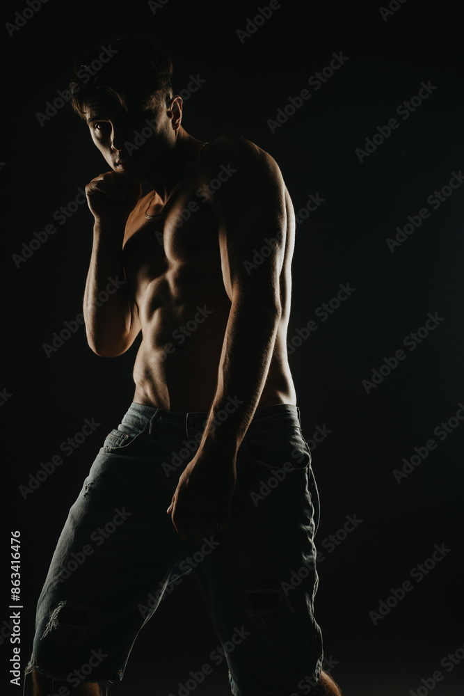 Shirtless muscular man posing confidently in low-light, highlighting toned abs and physique, wearing denim shorts. Shirtless muscular man posing confidently in low-light, highlighting toned abs and physique, wearing denim shorts.