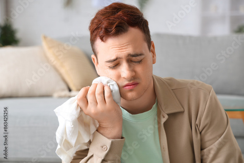 Young man with cold compress suffering from toothache in room