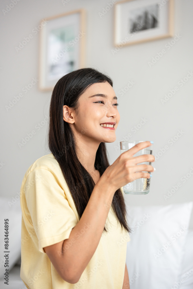 Asian attractive woman sit on bed, drink a glass of water in bedroom. Asian attractive woman sit on bed, drink a glass of water in bedroom.