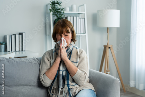 Caucasian senior woman having running nose and sneezing in living room.  photo