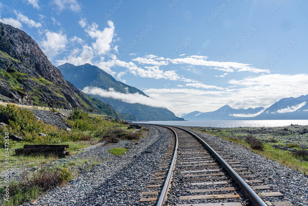 Fototapeta premium Railroad tracks running through Alaskan landscape with mountains and blue sky