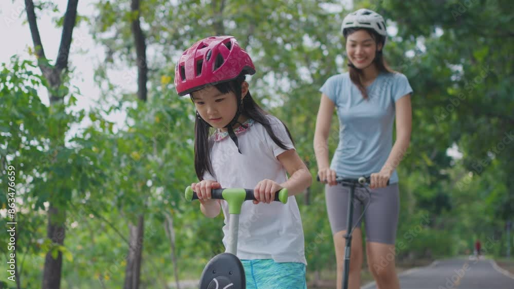 Asian young mother and daughter riding scooter outdoor in the garden. Asian young mother and daughter riding scooter outdoor in the garden.