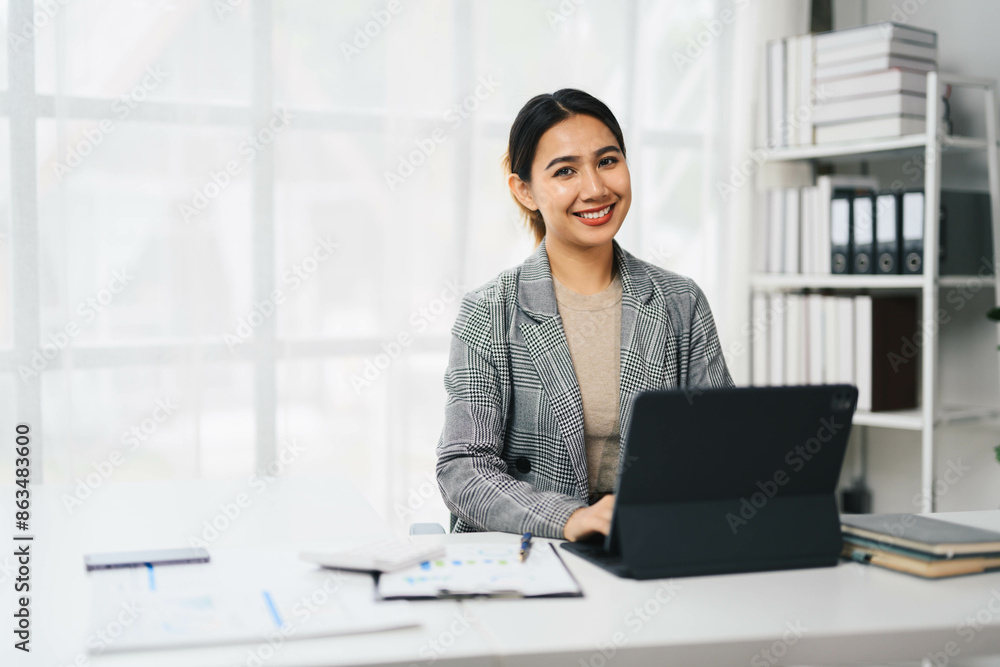 Confident Asian Business Woman Working on Laptop in Modern Office Setting with Documents and Books Confident Asian Business Woman Working on Laptop in Modern Office Setting with Documents and Books
