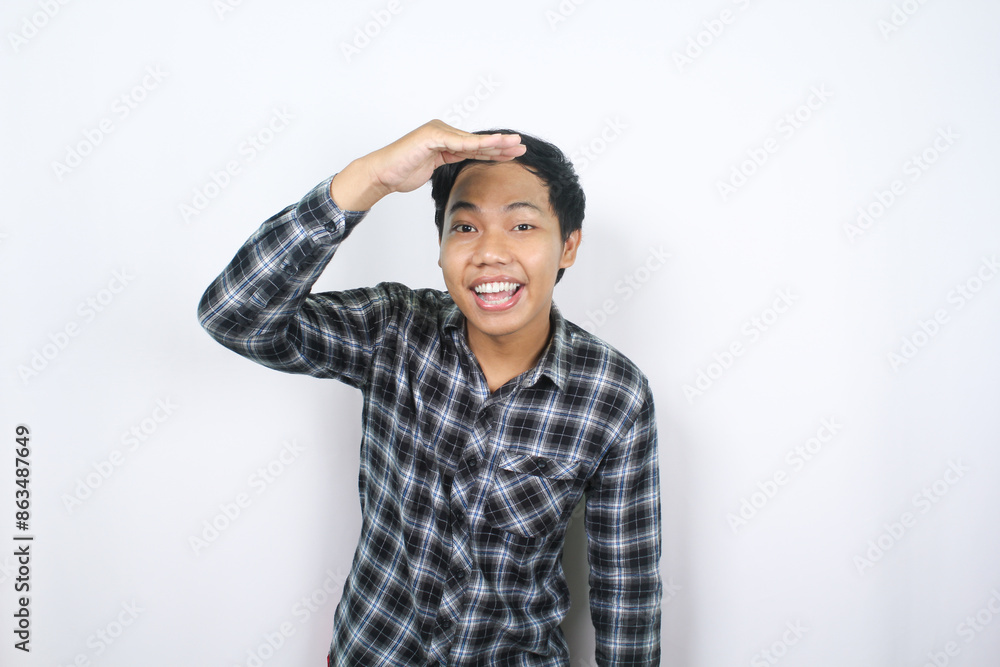 happy asian man in casual shirt posing look far away with raised hand over his head isolated happy asian man in casual shirt posing look far away with raised hand over his head isolated