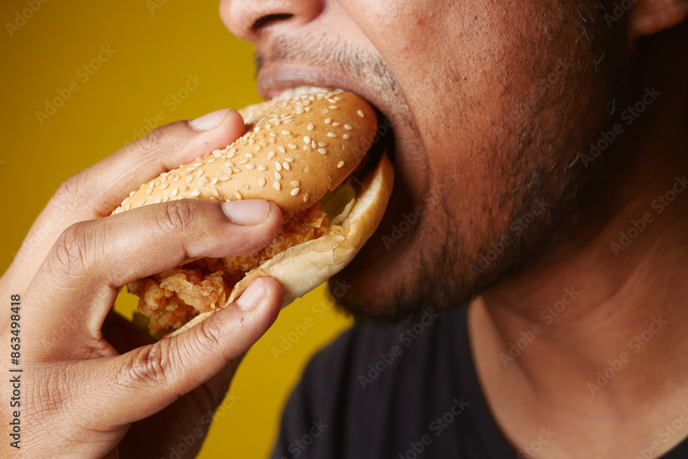 Man eating hamburger over yellow background Man eating hamburger over yellow background