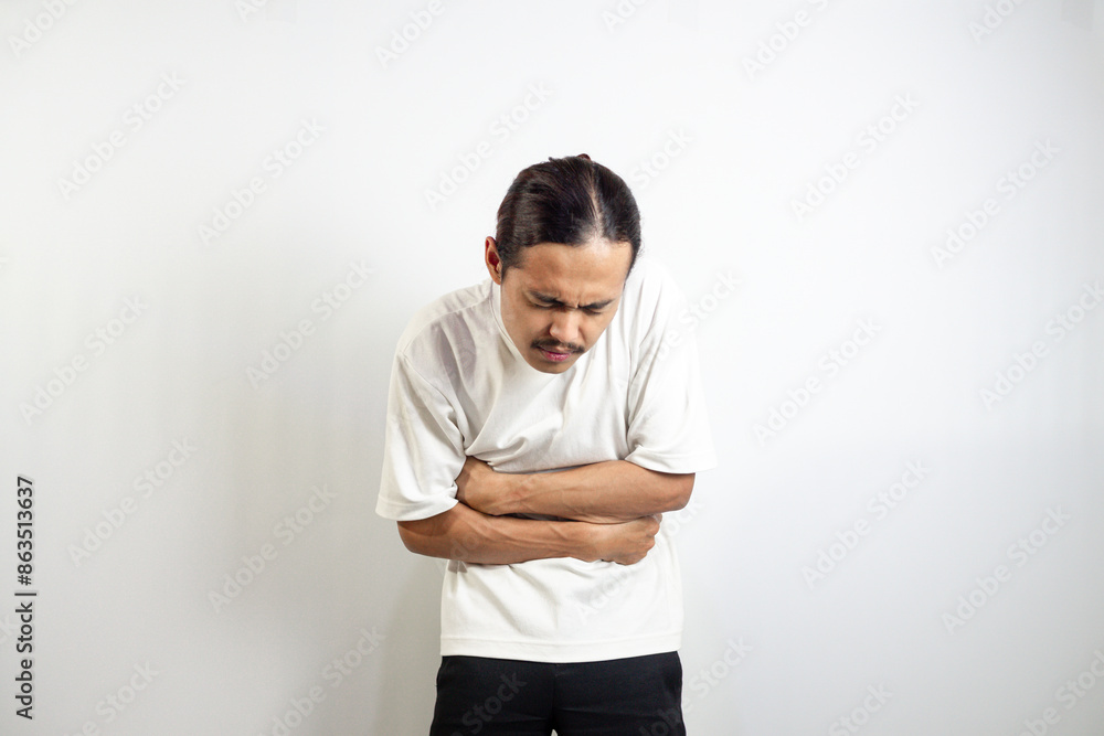 Young Asian man. suffering from severe stomach ache. isolated on white. Young Asian man. suffering from severe stomach ache. isolated on white.