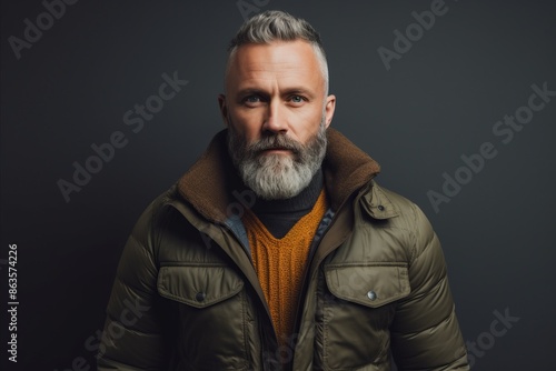 Portrait of a handsome middle-aged man with a gray beard in a warm jacket on a dark background