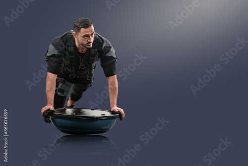 Young fit man in EMS suit doing push-ups with bosu ball, Active lifestyle: Electro muscle stimulator used by male model, ideal for workout inspiration photo