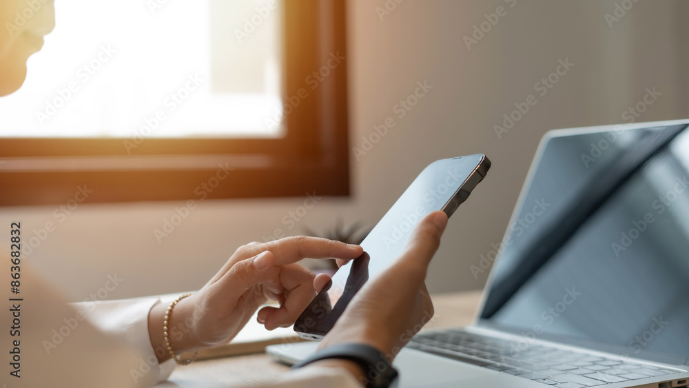 Fototapeta premium A woman is using a tablet and laptop computer at her desk. She is looking at the screen and touching the tablet