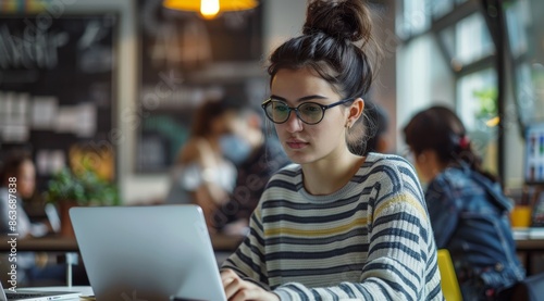 Young woman with glasses working on laptop in a cozy cafe environment