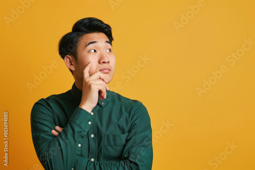 Pensive man in green shirt on solid yellow background