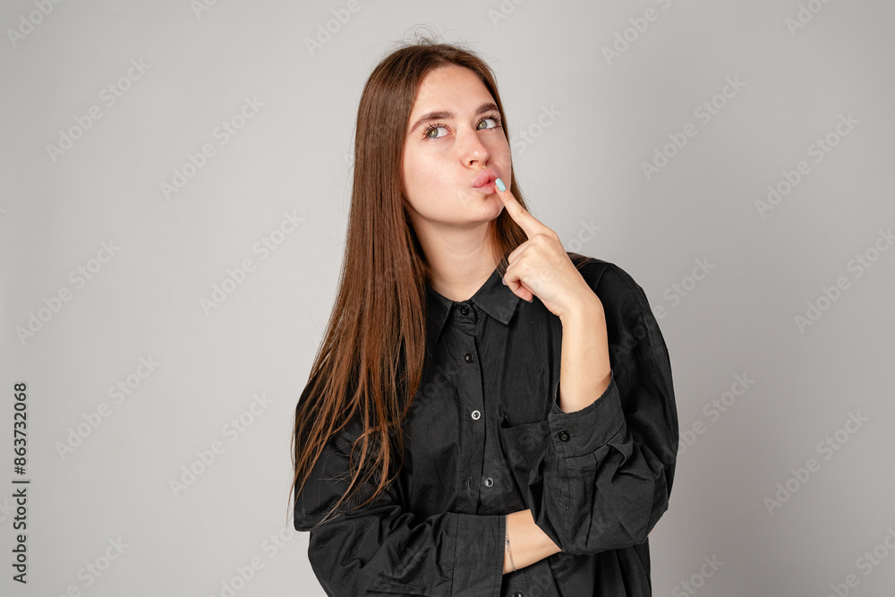 Young Woman In Black Shirt Pondering a Thought Against a Gray Backdrop Young Woman In Black Shirt Pondering a Thought Against a Gray Backdrop