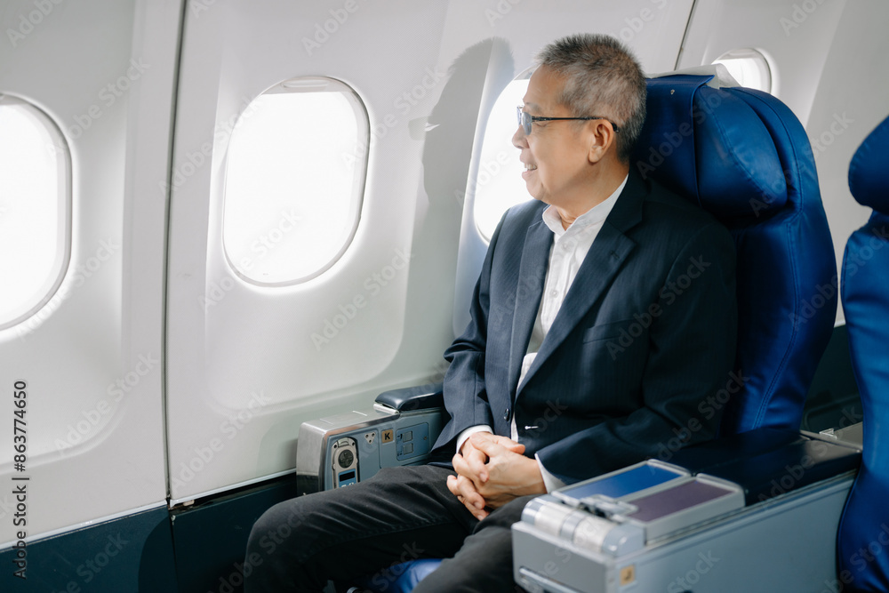 Asian Mature man sitting in a seat in airplane and looking out the window going on a trip vacation travel concept. using a phone, laptop Asian Mature man sitting in a seat in airplane and looking out the window going on a trip vacation travel concept. using a phone, laptop