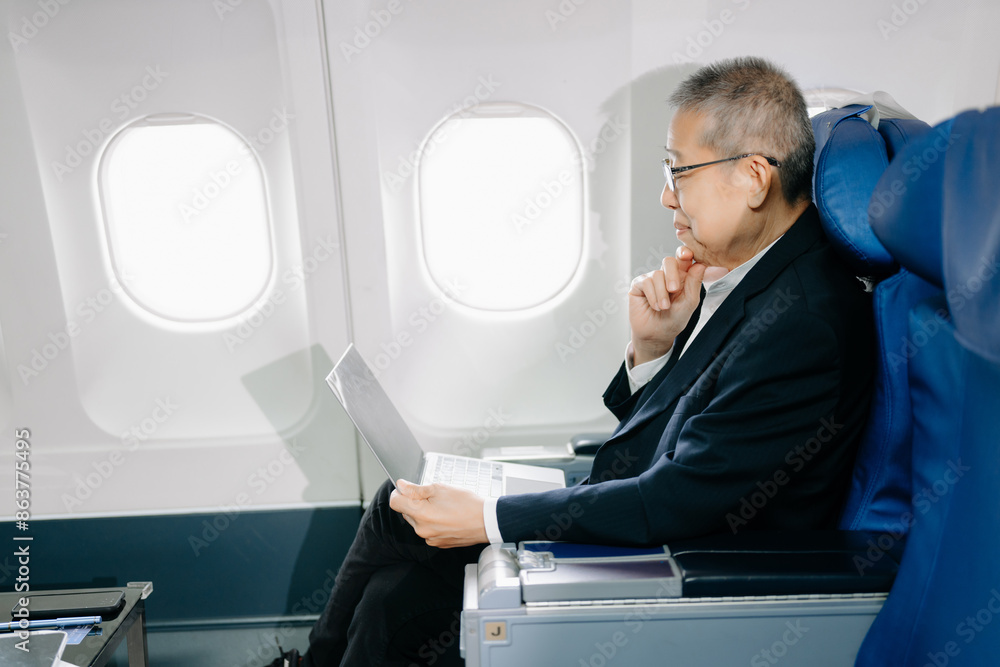 Asian Mature man sitting in a seat in airplane and looking out the window going on a trip vacation travel concept. using a phone, laptop Asian Mature man sitting in a seat in airplane and looking out the window going on a trip vacation travel concept. using a phone, laptop