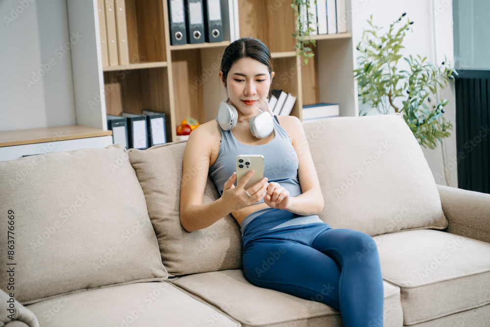 Young woman in fitness attire using a tablet on the couch with headphones around her neck. Experience modern, relaxed living. Young woman in fitness attire using a tablet on the couch with headphones around her neck. Experience modern, relaxed living.