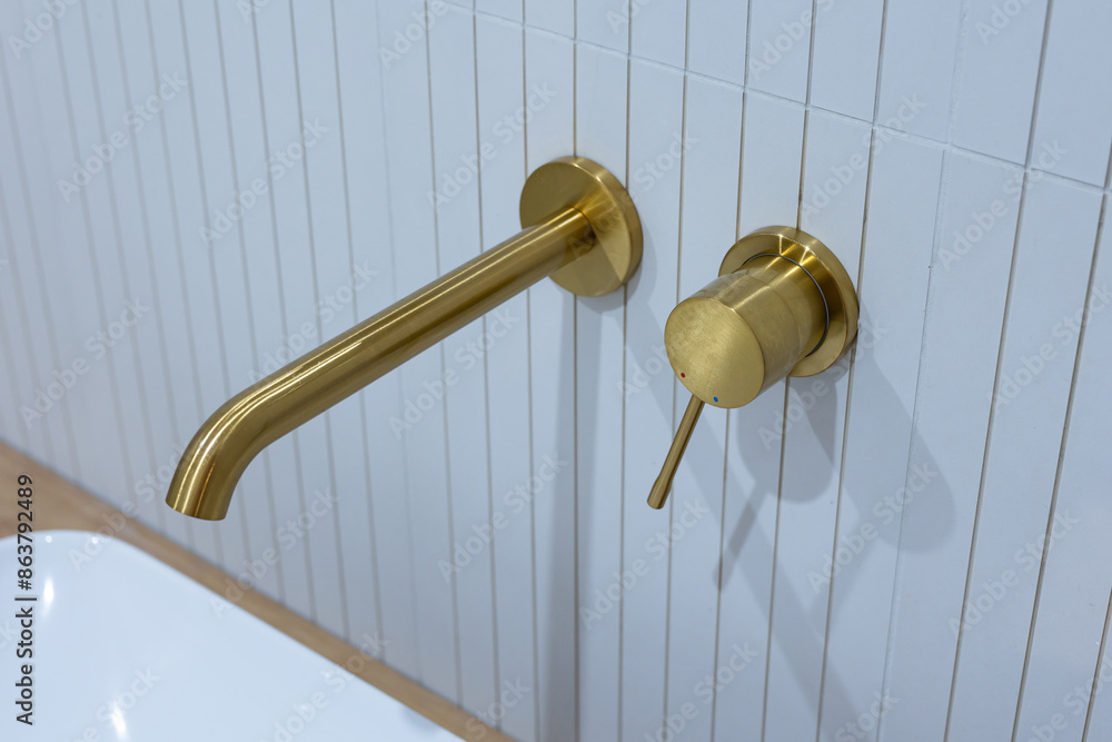 Bronze bathroom water tap in a bathroom finished with white tiles. Minimalist bathroom finish. Photographed in natural light.