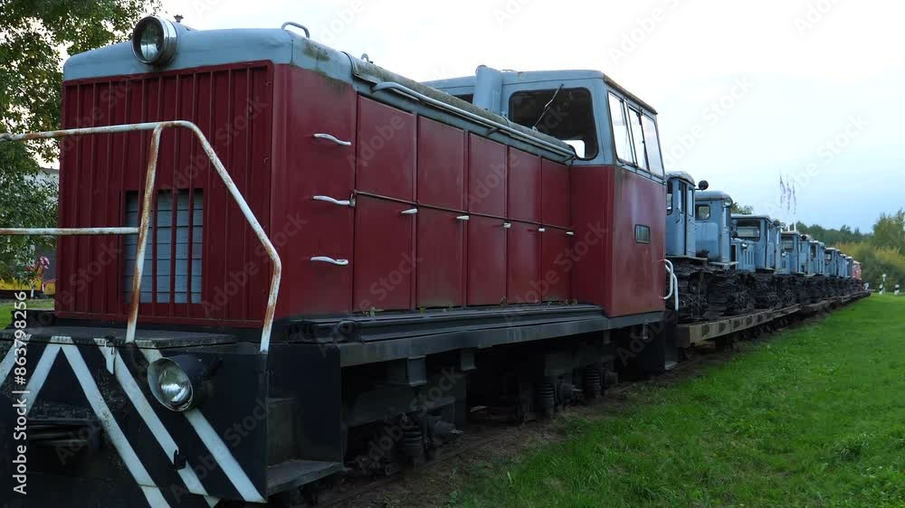 Old train locomotive or train engine and obsolete tracked tractors on platform on railroad in countryside next to road. Old train locomotive or train engine and obsolete tracked tractors on platform on railroad in countryside next to road.