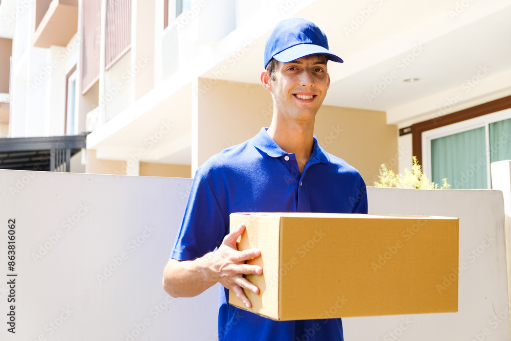 Delivery man in blue uniform. A male employee in a cap t-shirt working as courier dealer hold empty cardboard box. Young courier holding parcels on doorstep. Delivery service concept Delivery man in blue uniform. A male employee in a cap t-shirt working as courier dealer hold empty cardboard box. Young courier holding parcels on doorstep. Delivery service concept