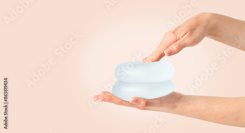 Hand pressing soft breast implant in hand on beige background, copy space.
