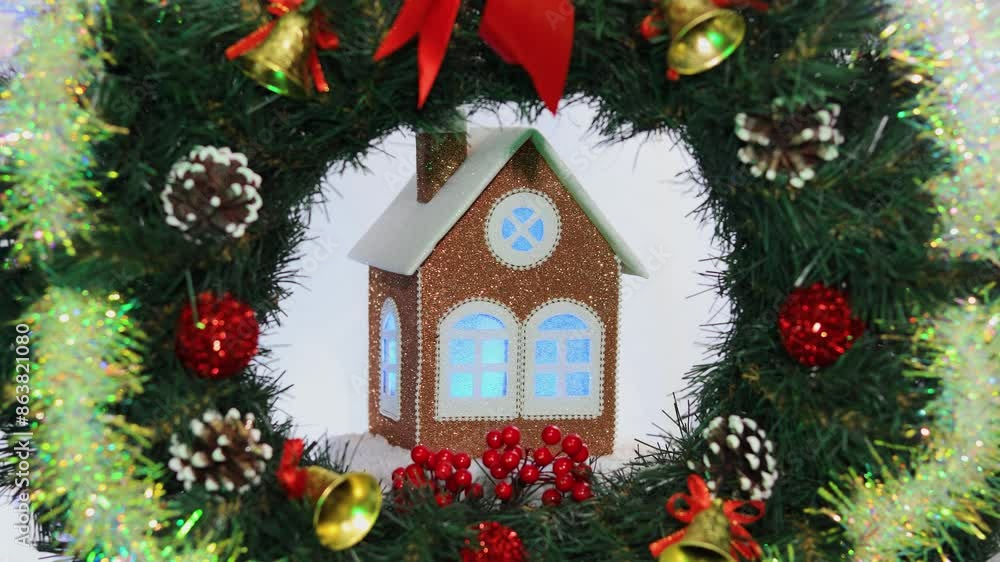 In the middle of a decorated Christmas wreath, a brown Christmas decorated house rotates on a white background In the middle of a decorated Christmas wreath, a brown Christmas decorated house rotates on a white background