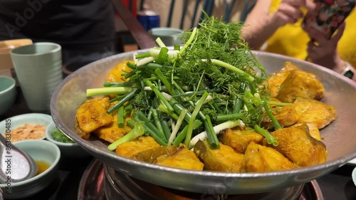 A professional chef using chopsticks to adds cilantro and spring onion to the traditional and popular dish of boneless grilled hemibagrus fish, known as Cha Ca Hanoi, a fried river catfish.