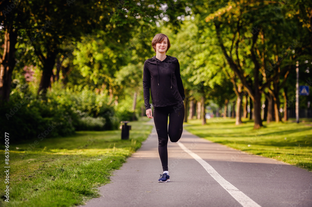 A young woman in black sportswear stretching her leg on a park path before running. Highlighting warm-up routines and a healthy outdoor lifestyle. A young woman in black sportswear stretching her leg on a park path before running. Highlighting warm-up routines and a healthy outdoor lifestyle.