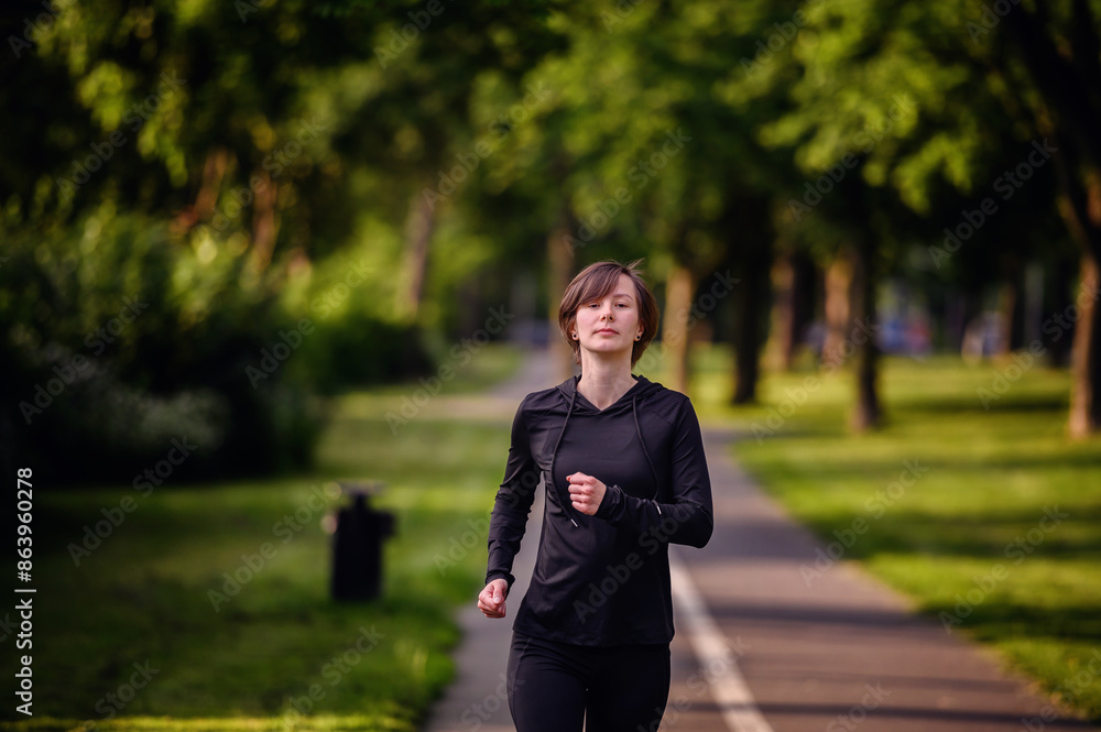 A young woman in black sportswear running on a park path, surrounded by lush greenery. Showcasing fitness, determination, and a healthy outdoor lifestyle. A young woman in black sportswear running on a park path, surrounded by lush greenery. Showcasing fitness, determination, and a healthy outdoor lifestyle.