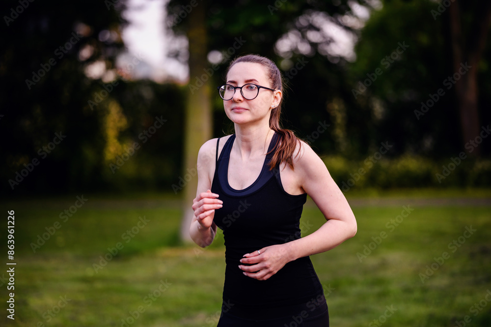 A young woman in black sportswear and glasses jogging in a park, showcasing determination and a healthy lifestyle. A young woman in black sportswear and glasses jogging in a park, showcasing determination and a healthy lifestyle.