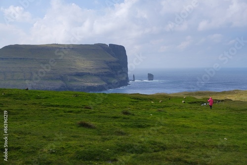 Silhouette of tourist on viewpoint with famous Risin and Kellingin sea stacks by cliff of Eysturoy Island on horizon. Faroe Islands, Denmark.  photo